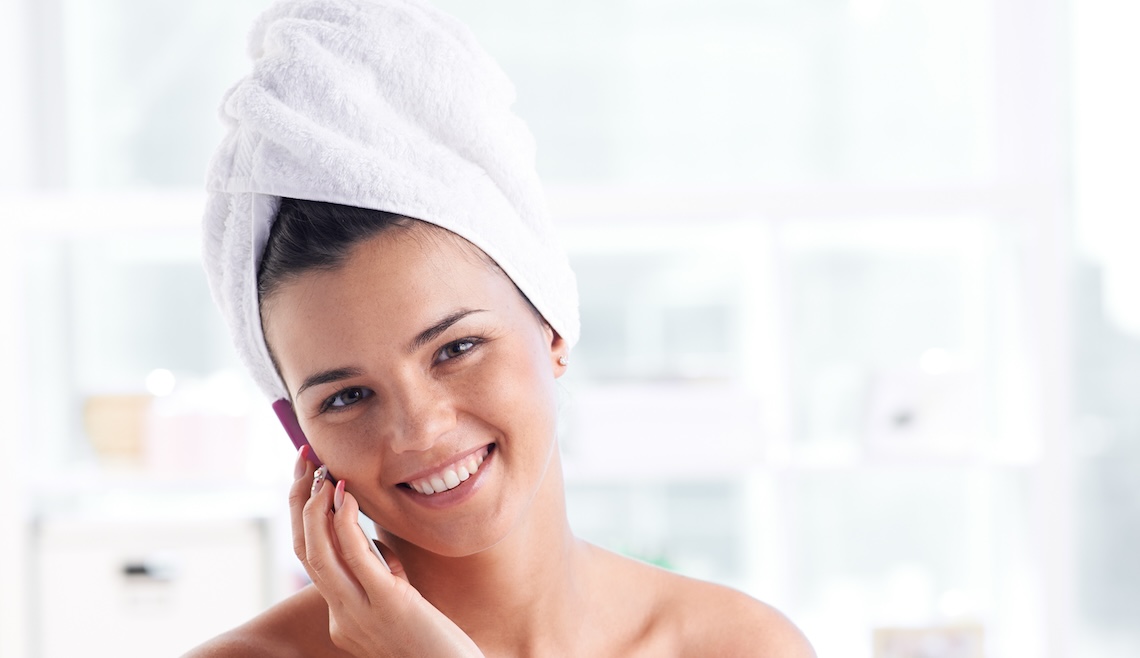 Girl with a towel on her head and body speaking by the phone and looking at camera