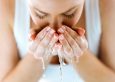 Portrait of beautiful young woman washing her face splashing water in a home bathroom.