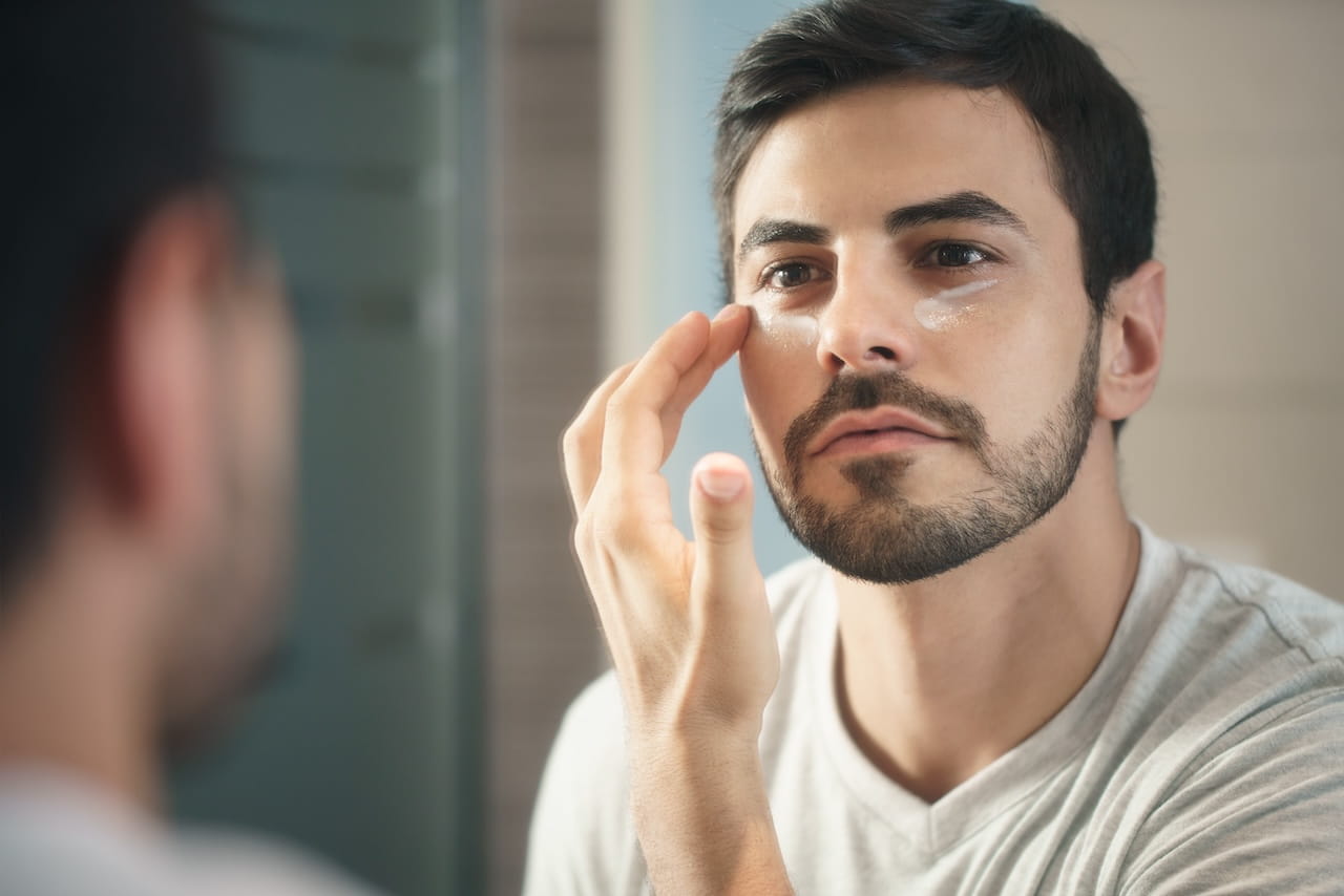 Young Man Applying Anti-aging Lotion fotr Skin Care. Young hispanic people and male beauty. Man applying lotion for anti-aging treatment around eye