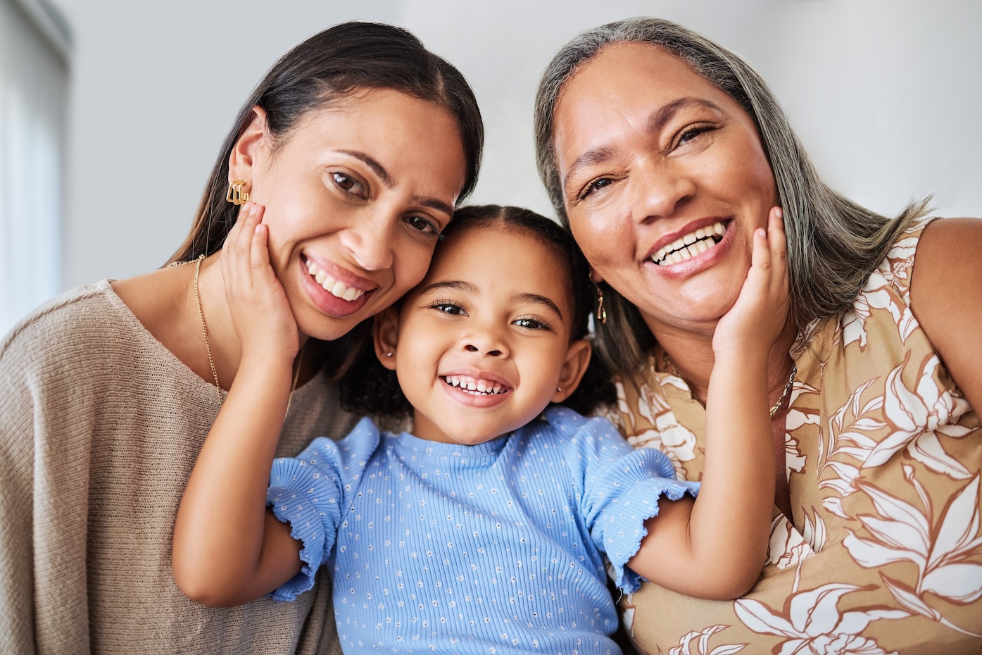 Mother, girl and grandma bond in living room, smile, relax and hug in their home. Face, portrait and happy family of multigenerational women hug, laugh and enjoying quality time at home together.
